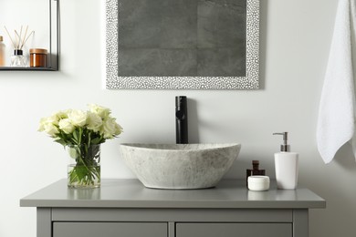 Photo of Vase with beautiful white roses and toiletries near sink in bathroom