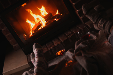 Couple and glasses of red wine near burning fireplace, closeup