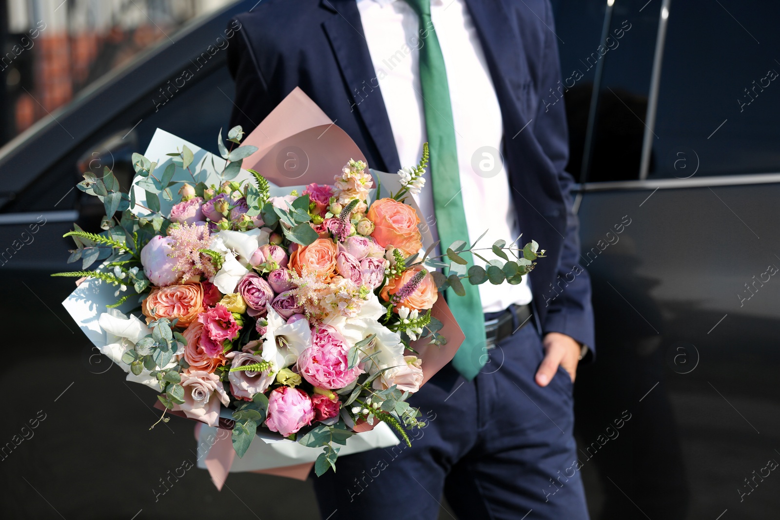 Photo of Man in stylish suit with beautiful flower bouquet near car on street, closeup view