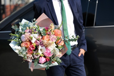 Photo of Man in stylish suit with beautiful flower bouquet near car on street, closeup view