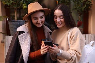 Photo of Happy friends with smartphone and paper cups outdoors