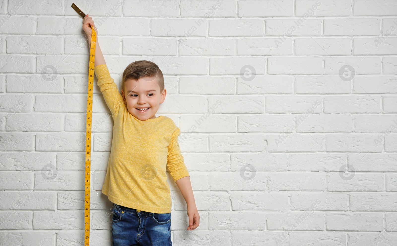 Photo of Little boy measuring his height on brick wall background