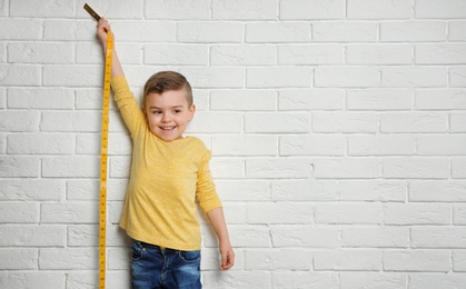 Little boy measuring his height on brick wall background