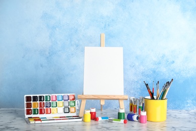 Wooden easel with blank canvas board and painting tools for children on table near color wall