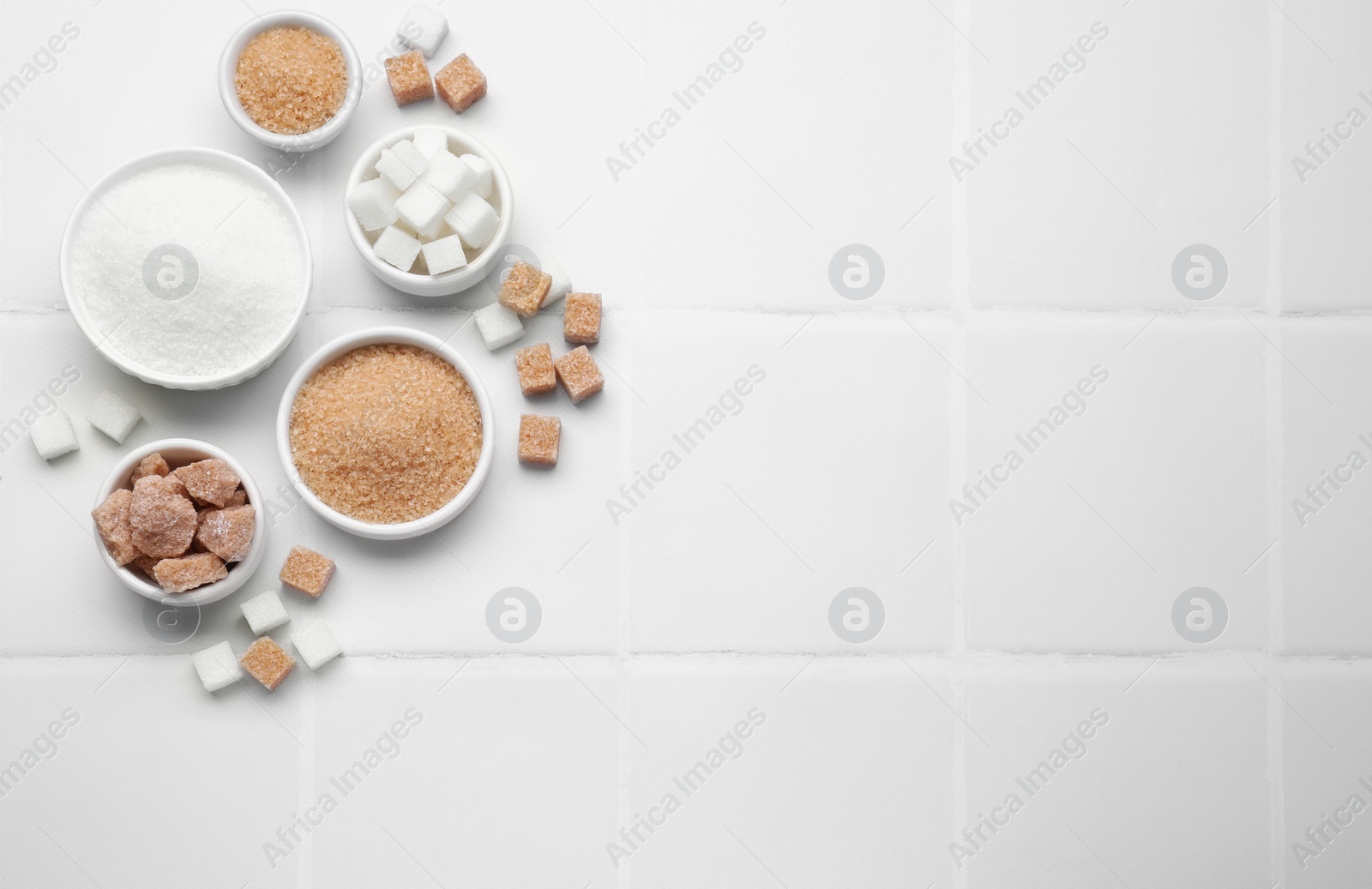 Photo of Different types of sugar on white tiled table, flat lay. Space for text