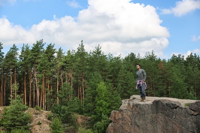 Young man on rock near beautiful forest. Camping season