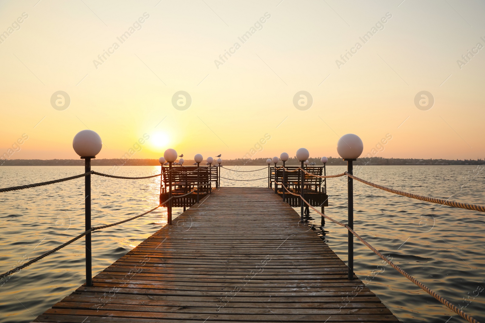 Photo of Picturesque view of empty wooden pier with lanterns at sunset