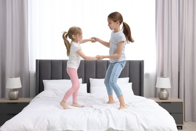 Cute little sisters having fun together on bed at home