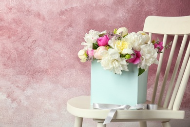 Box with bouquet of beautiful flowers on wooden chair against color background