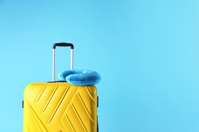 Photo of Yellow suitcase and travel pillow on light blue background, space for text