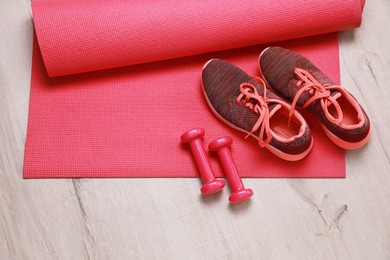 Photo of Dumbbells, sneakers and mat on wooden floor, above view