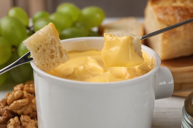 Photo of Dipping pieces of bread into tasty cheese fondue on table, closeup view