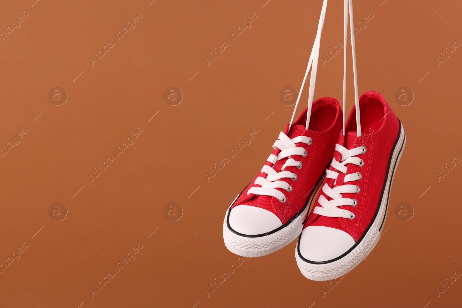 Photo of Pair of red classic old school sneakers on brown background. Space for text