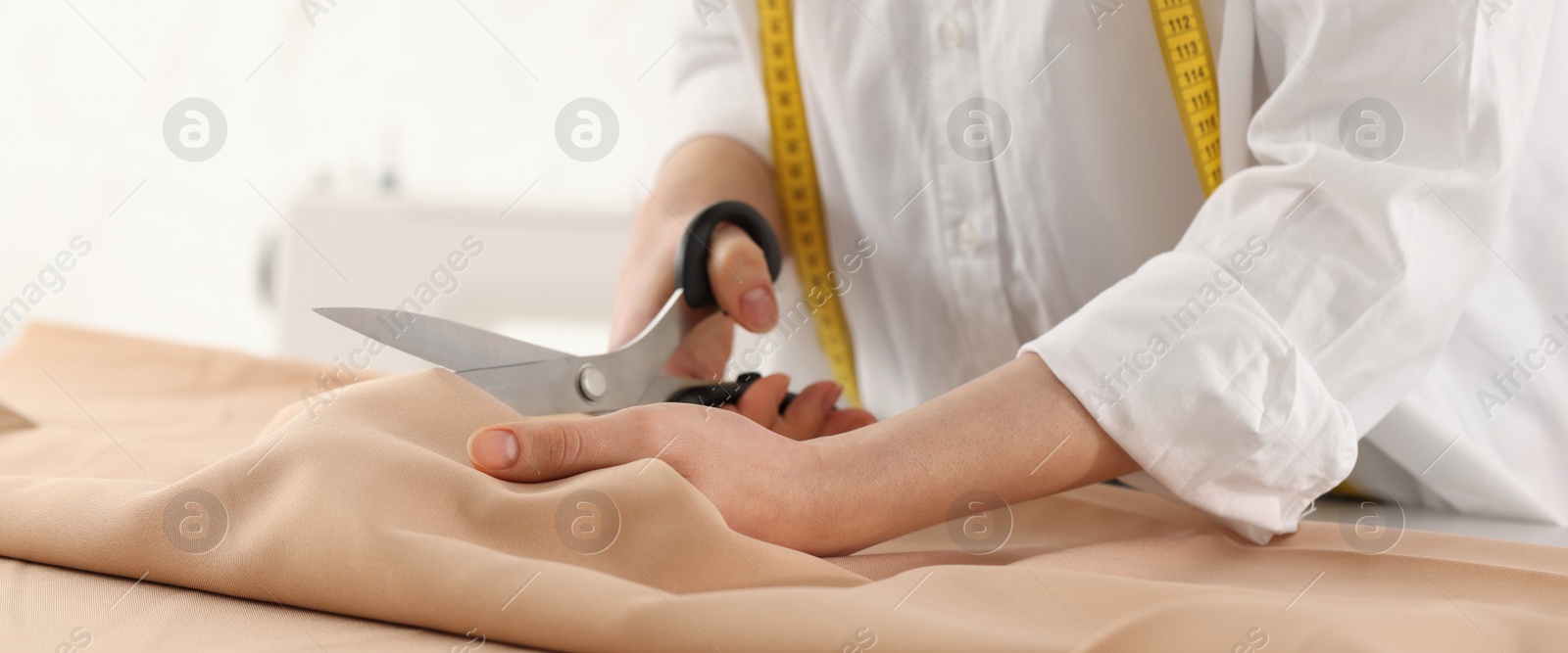 Image of Dressmaker cutting fabric with scissors at table in workshop, closeup. Banner design