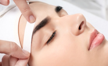 Photo of Young woman having professional eyebrow correction procedure in beauty salon, closeup