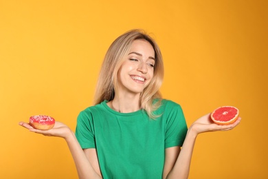 Photo of Woman choosing between doughnut and healthy grapefruit on yellow background