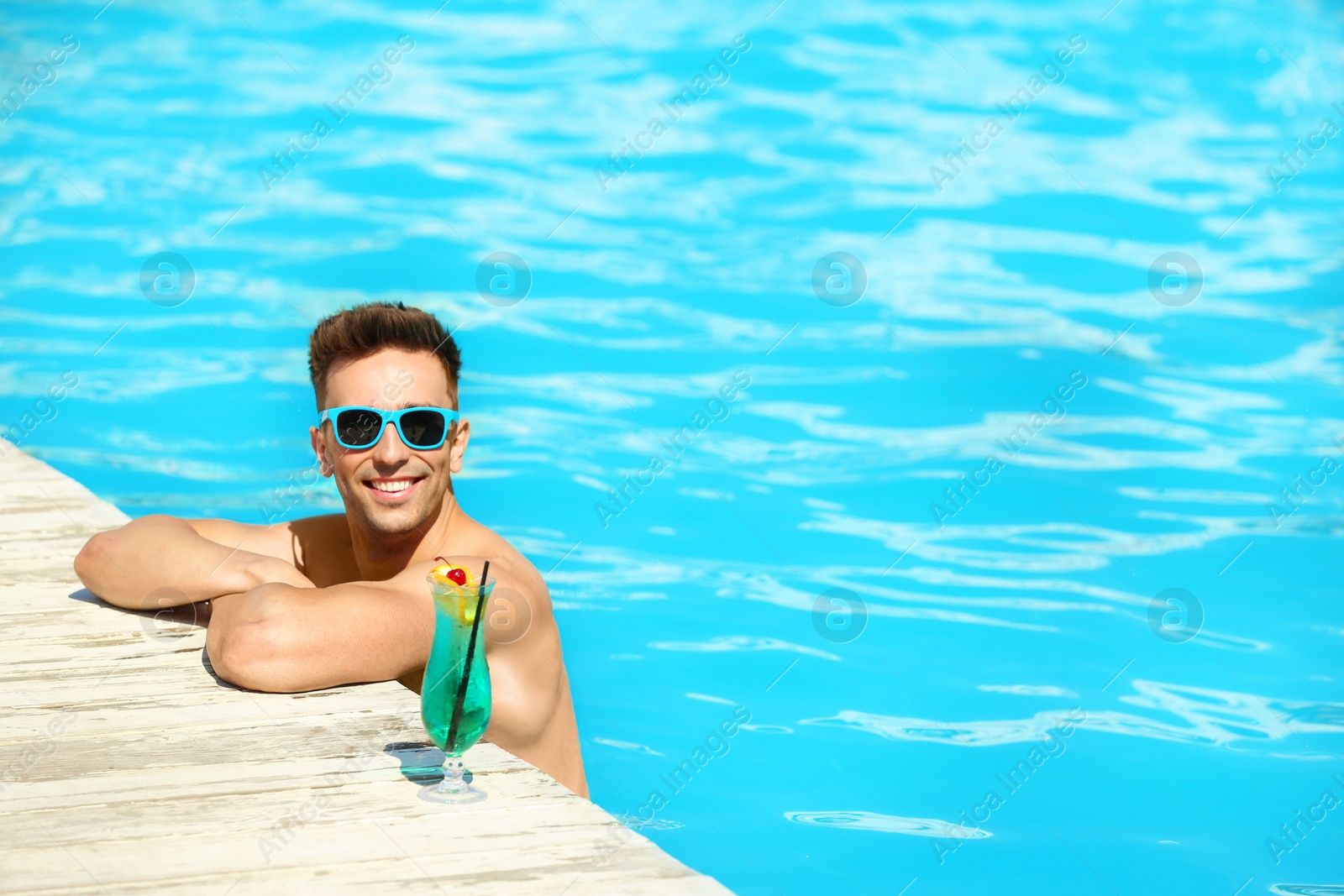 Photo of Happy young man with cocktail in swimming pool