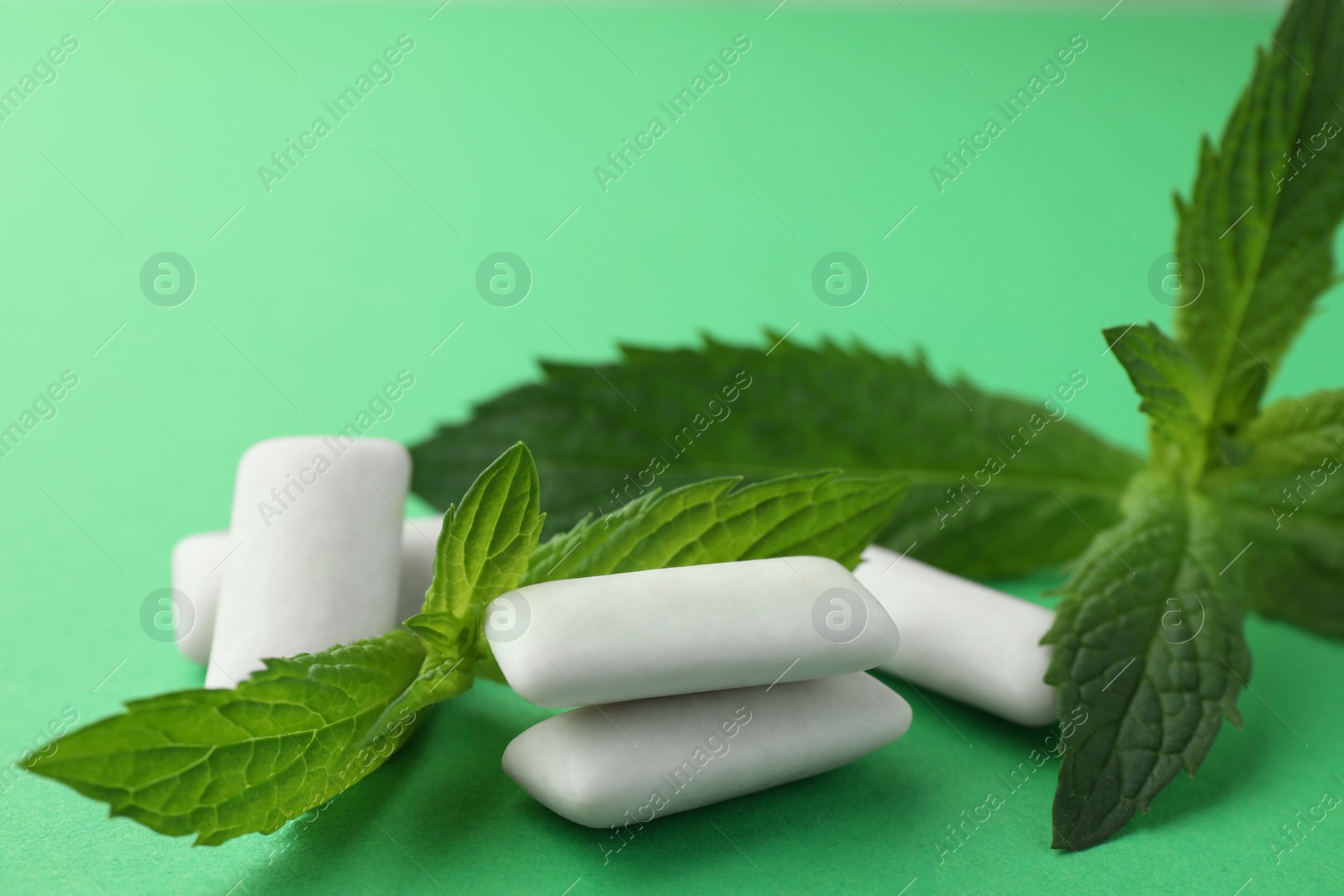 Photo of Tasty white chewing gums and mint leaves on green background, closeup