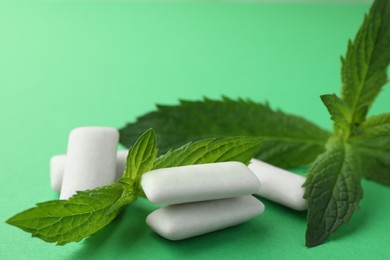 Tasty white chewing gums and mint leaves on green background, closeup