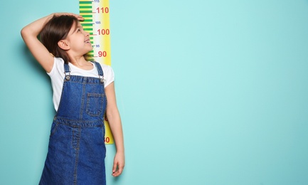 Little girl measuring her height on color background