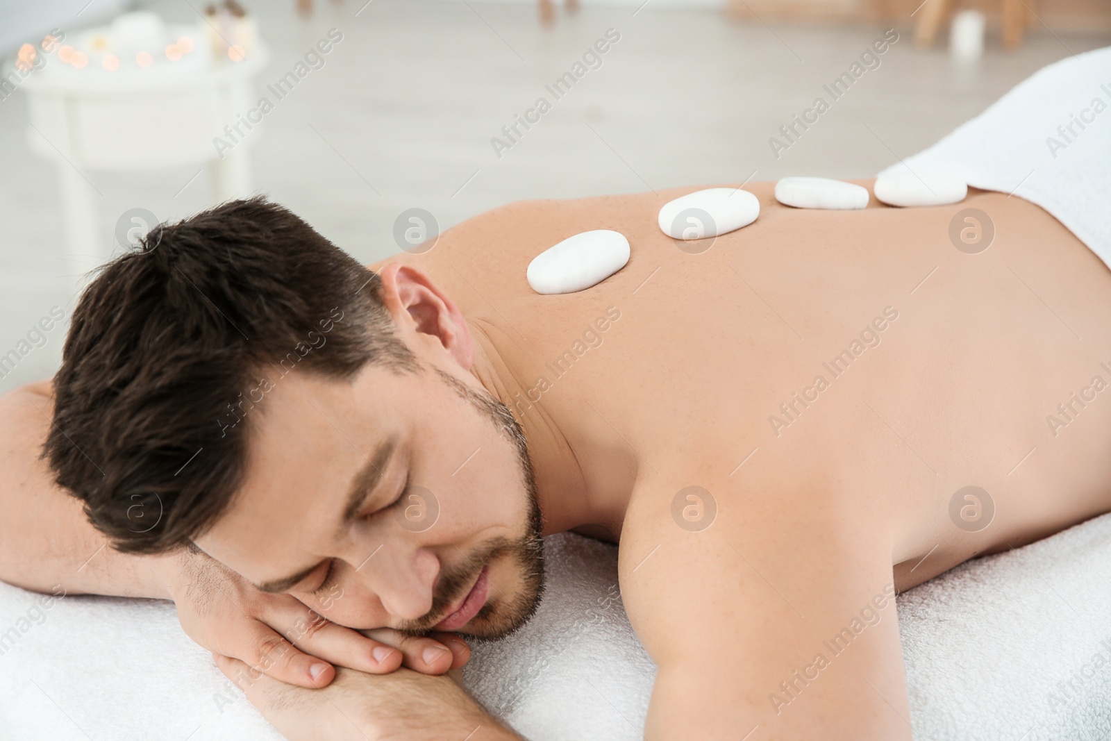 Photo of Handsome man receiving hot stone massage in spa salon