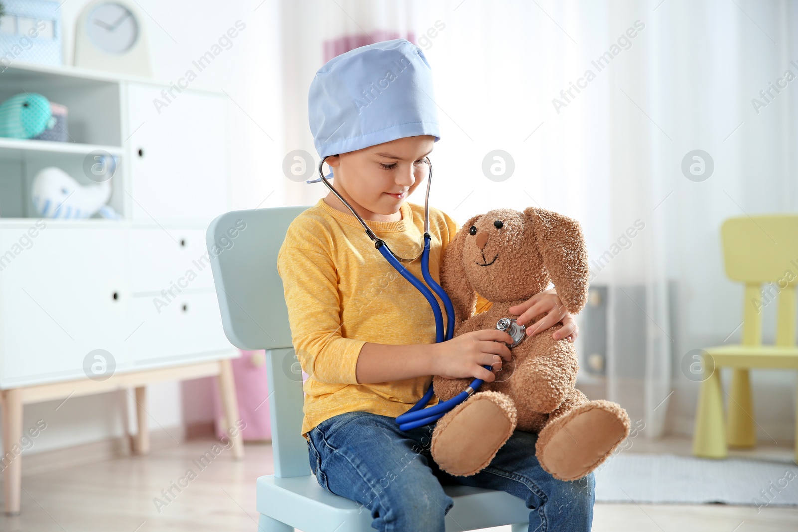 Photo of Cute child imagining himself as doctor while playing with stethoscope and toy bunny at home