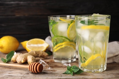 Glasses of refreshing drink with lemon and mint on wooden table against dark background, space for text