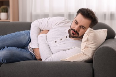 Photo of Man suffering from stomach pain on sofa at home