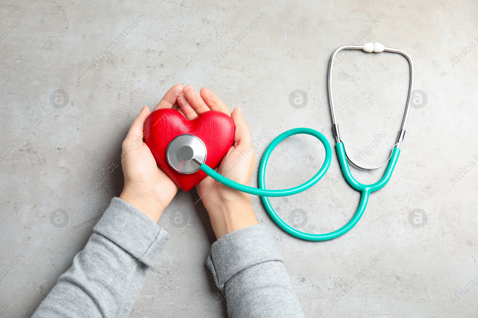 Photo of Woman holding red heart and stethoscope on gray background, top view. Cardiology concept