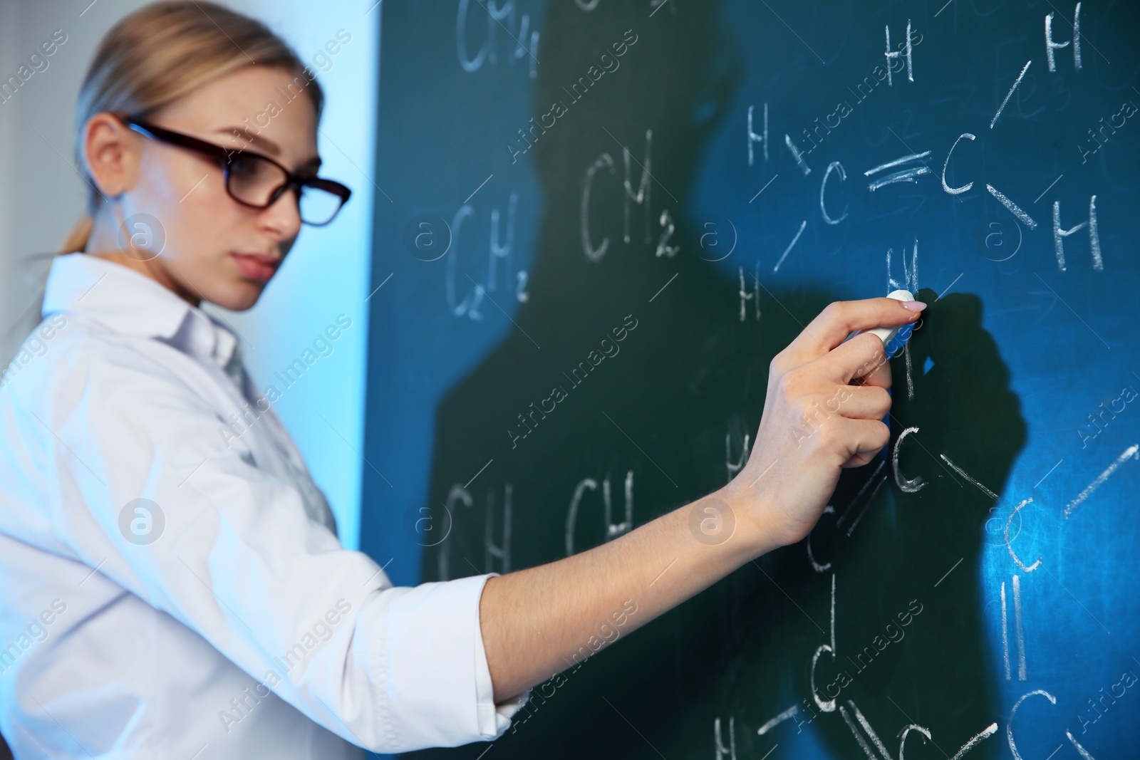 Photo of Female scientist writing chemical formula on chalkboard indoors