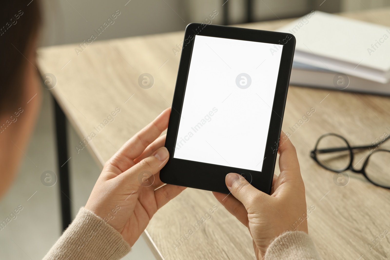 Photo of Young woman using e-book reader at wooden table indoors, closeup