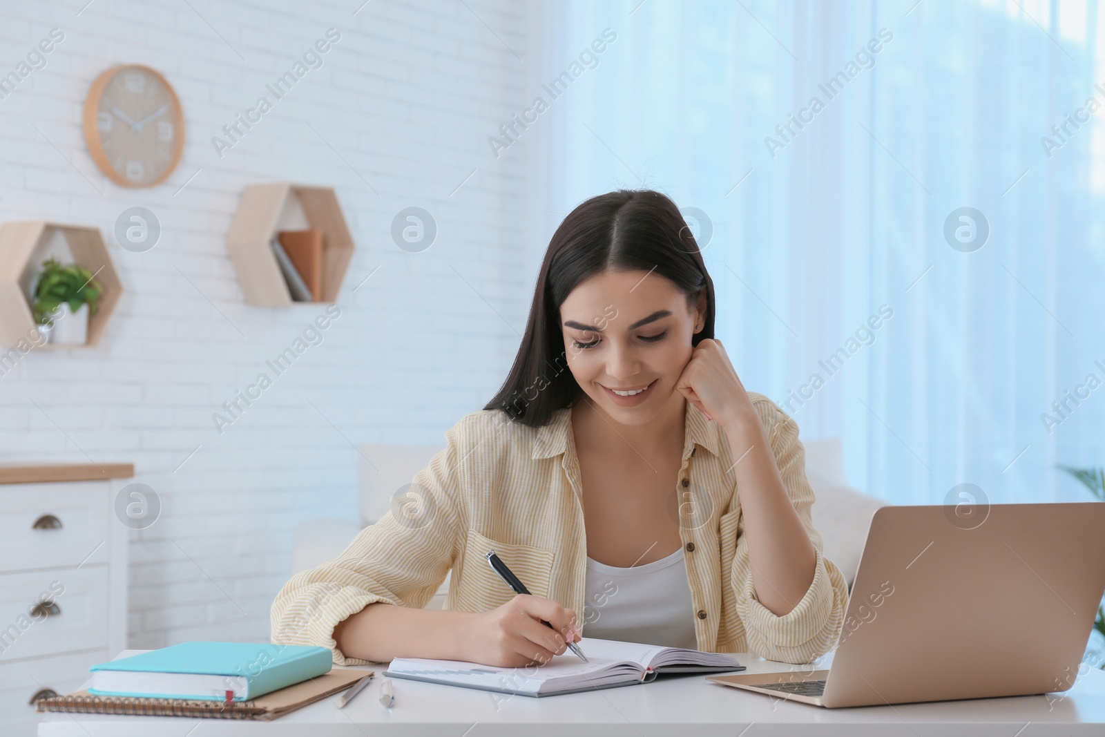 Photo of Young woman taking notes during online webinar at table indoors