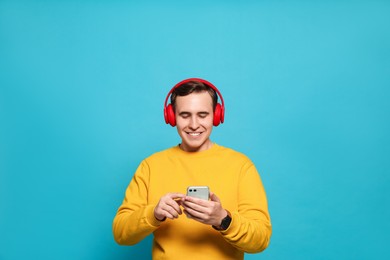 Photo of Handsome young man with headphones and modern smartphone on light blue background