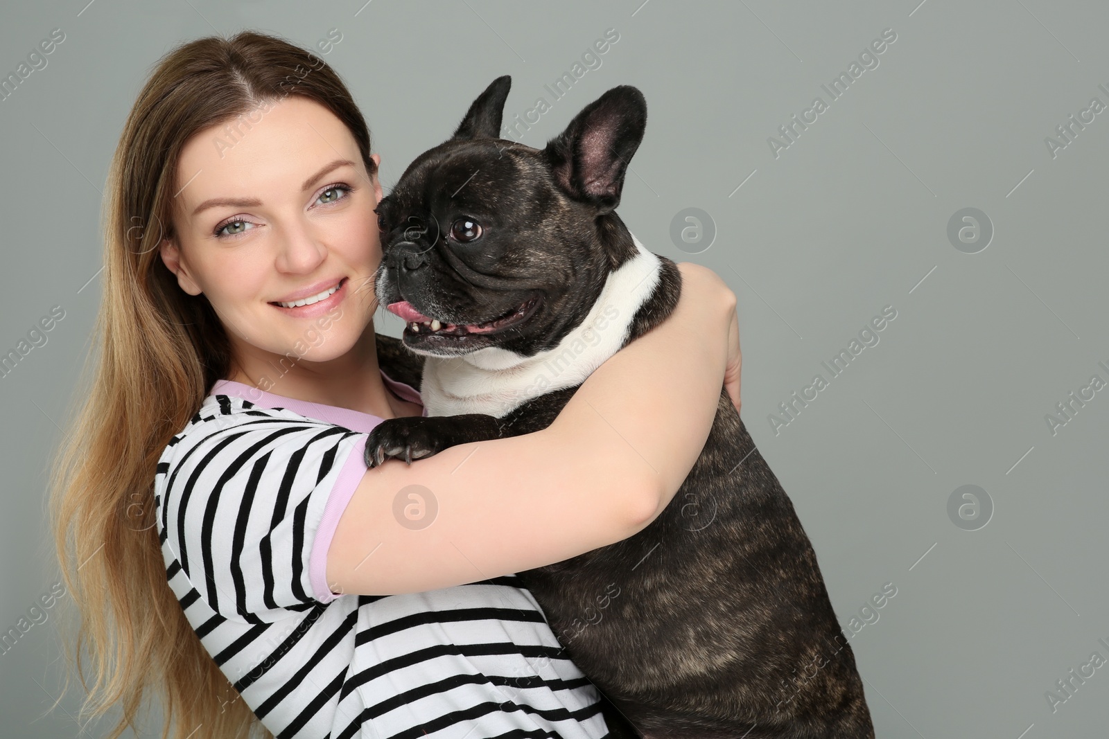 Photo of Portrait of happy woman hugging cute French Bulldog on grey background