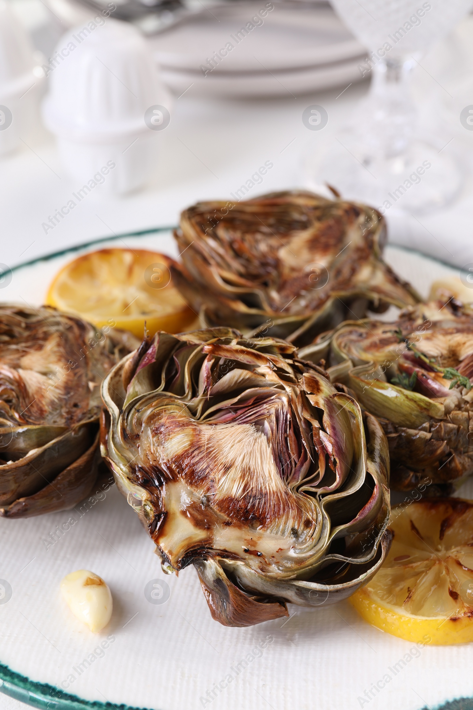 Photo of Plate with tasty grilled artichokes on white table, closeup