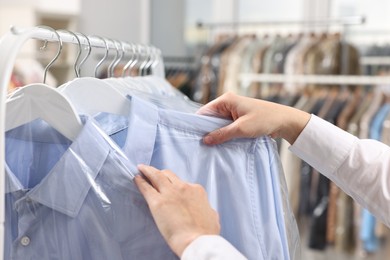 Photo of Dry-cleaning service. Woman taking shirt in plastic bag from rack indoors, closeup