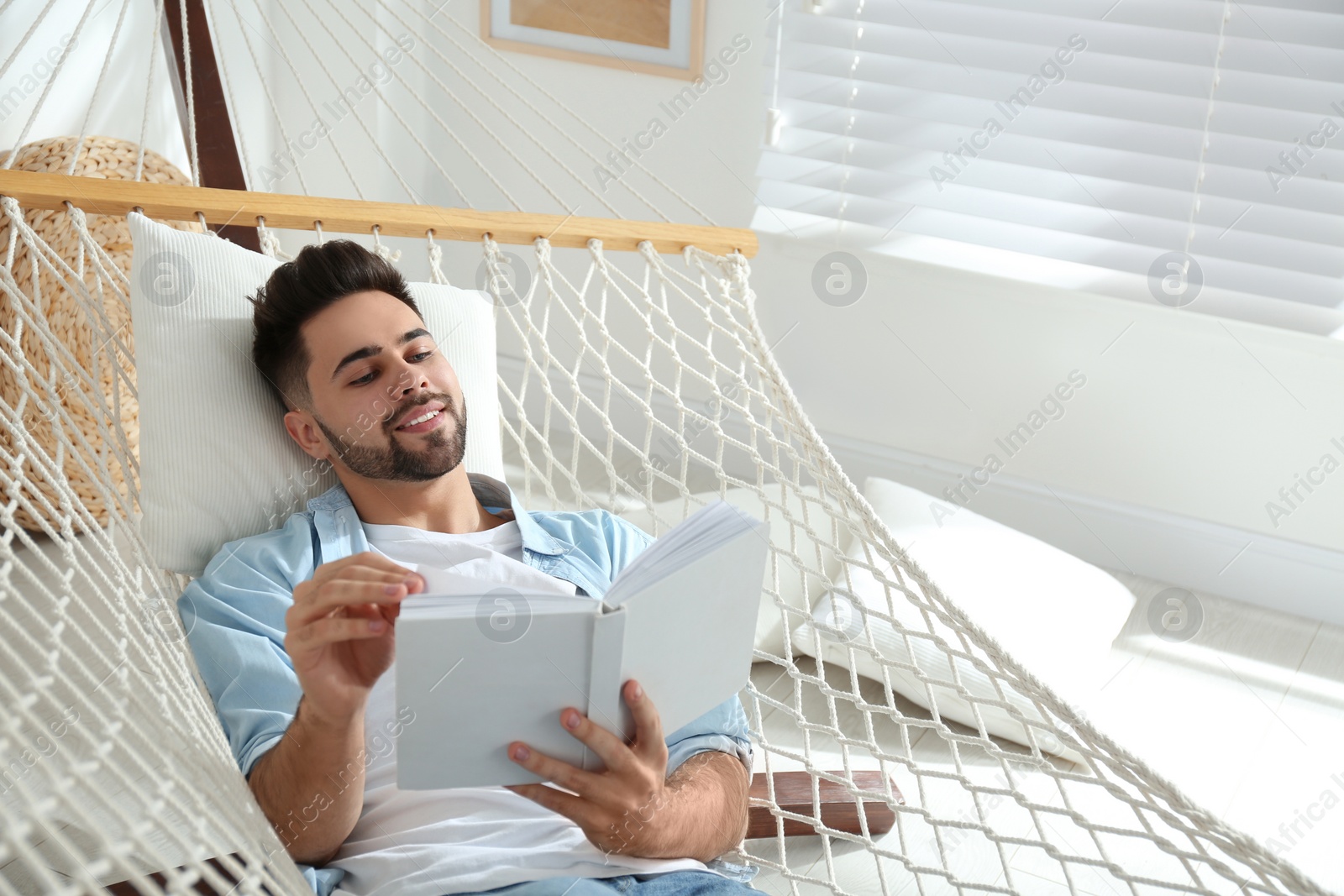 Photo of Young man reading book in hammock at home