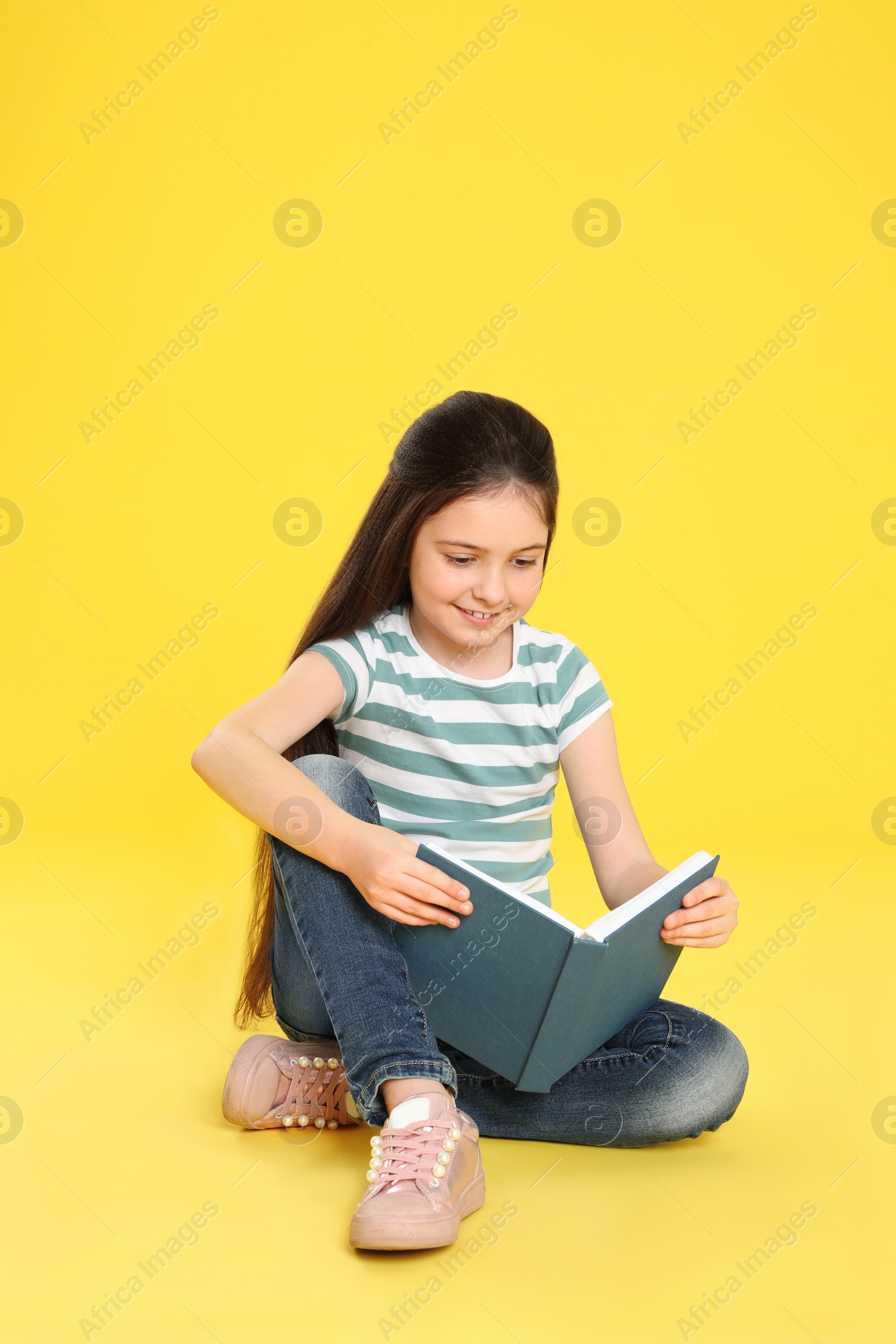 Photo of Cute little girl reading book on color background, space for text