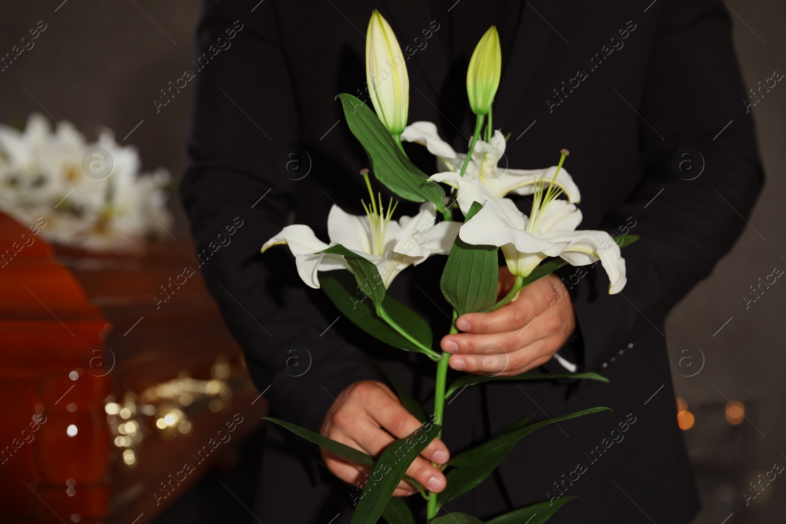 Photo of Young man with white lilies in funeral home, closeup