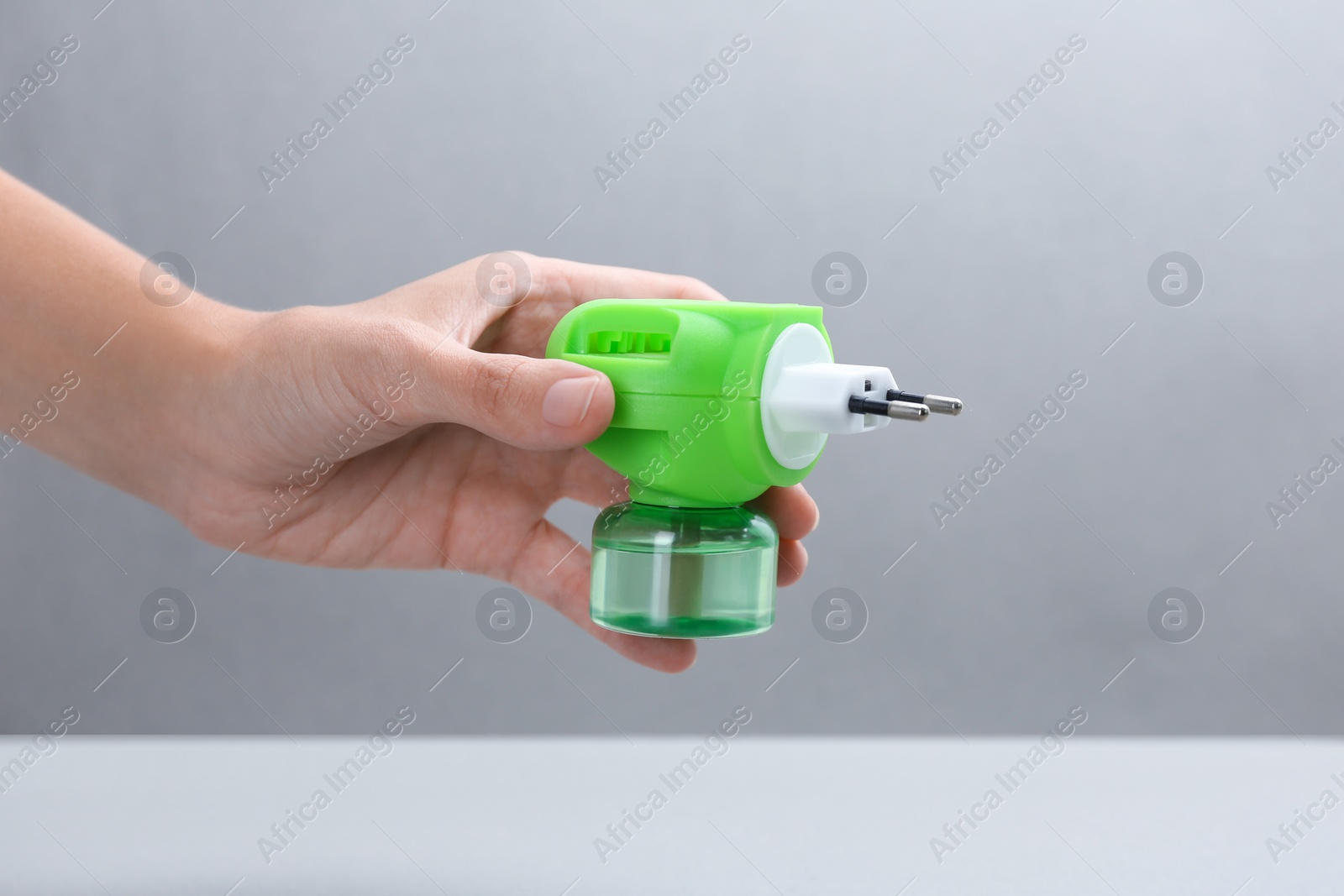 Photo of Woman holding electric vaporizer with insect repellent liquid on grey background, closeup