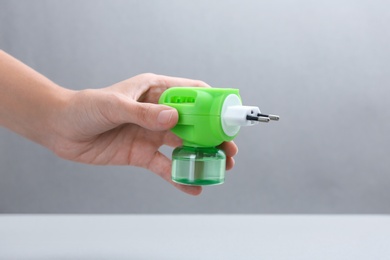 Photo of Woman holding electric vaporizer with insect repellent liquid on grey background, closeup