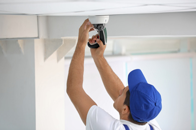 Photo of Technician installing CCTV camera on ceiling indoors