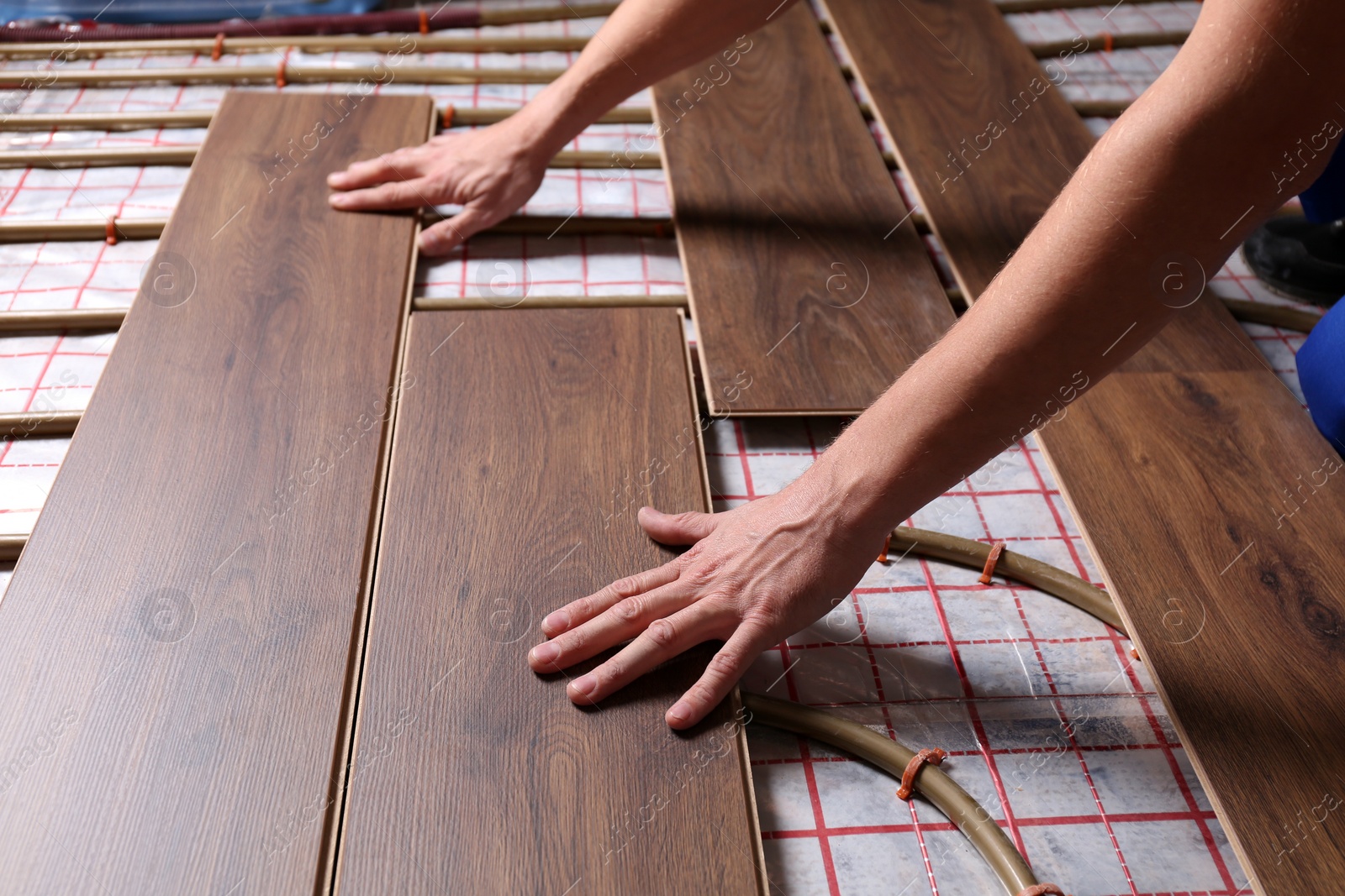 Photo of Worker installing new wooden laminate over underfloor heating system, closeup