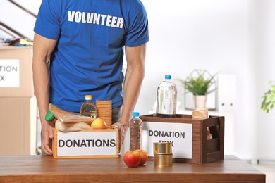 Photo of Male volunteer holding donation box with food products indoors