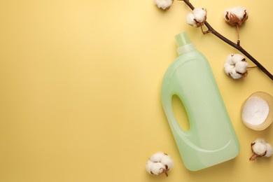 Photo of Bottle of fabric softener, detergent powder and cotton flowers on pale yellow background, flat lay. Space for text