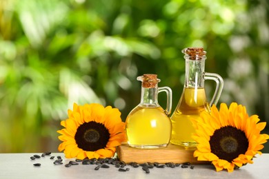 Photo of Sunflower cooking oil, seeds and yellow flowers on light grey table outdoors, space for text