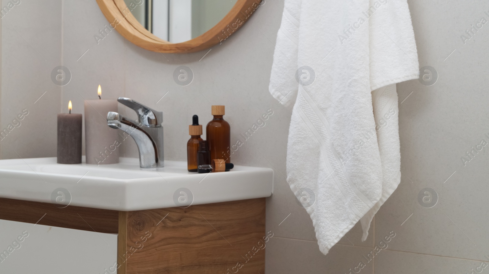 Photo of Hanging towel, sink, burning candles and toiletries in bathroom. Interior design