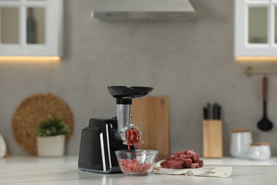 Photo of Electric meat grinder with beef mince on white table in kitchen, space for text