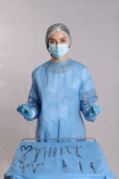 Doctor holding medical clamps near table with different surgical instruments on light background