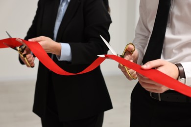 Photo of People cutting red ribbon with scissors on blurred background, closeup
